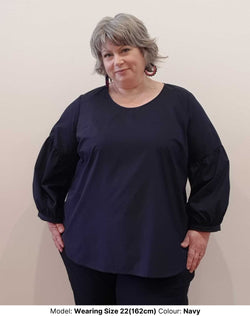 Plus Size Blouse in Navy Silk Blend Fabric with A Drop Puff Sleeve, a bit like a pirate. The blouse has a curved neckline and hemline. The sleeves are alrmost full length and finished in bangle style. The model is wearing size 24 top and size 24 Work pants for curvy bums in Navy