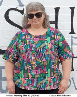 Bright Watercolour print blouse in plus sizes. The print is predominately green, pink, white, blue and yellow and looks very cheerful against a black background. The blouse is by Chasing Springtime and the model is wearing size 22