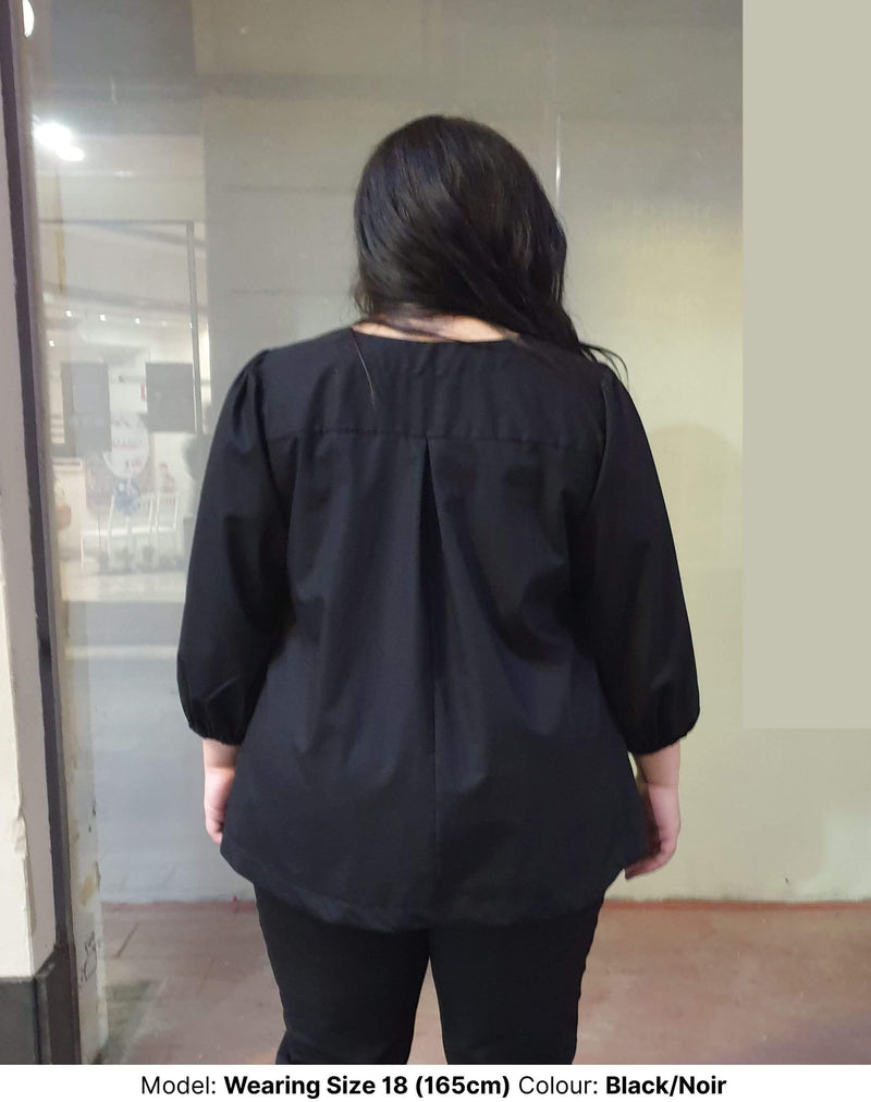 Plus size woman wearing black/noir work blouse facing the back